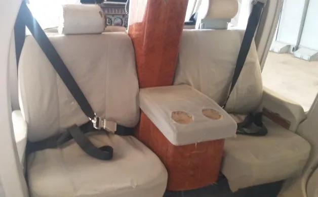 Close-up view of two light-colored cabin seats with seatbelts and a central console with cup holders inside the helicopter.