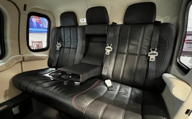 A row of three black leather passenger seats with red stitching inside a helicopter cabin.