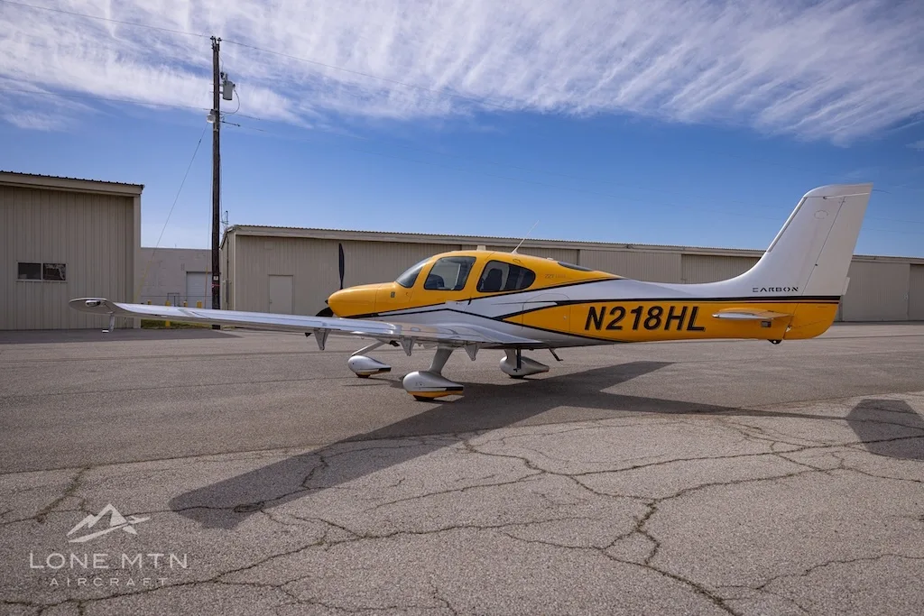 A Cirrus SR22 aircraft with yellow and silver paint scheme parked on an airfield, showing the left side.