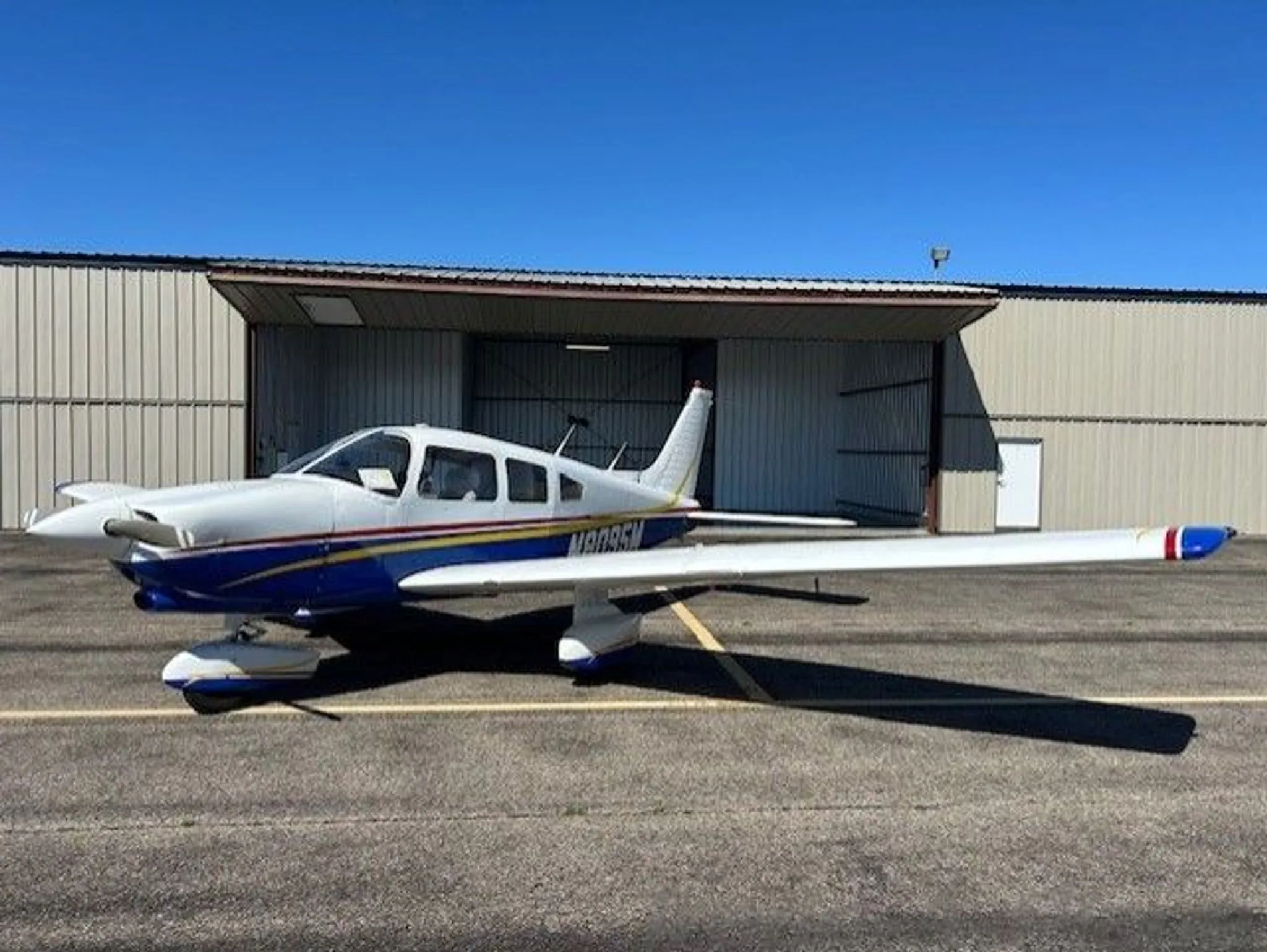 A side view of a white and blue Piper Cherokee aircraft with N8095M registration parked on an airfield.