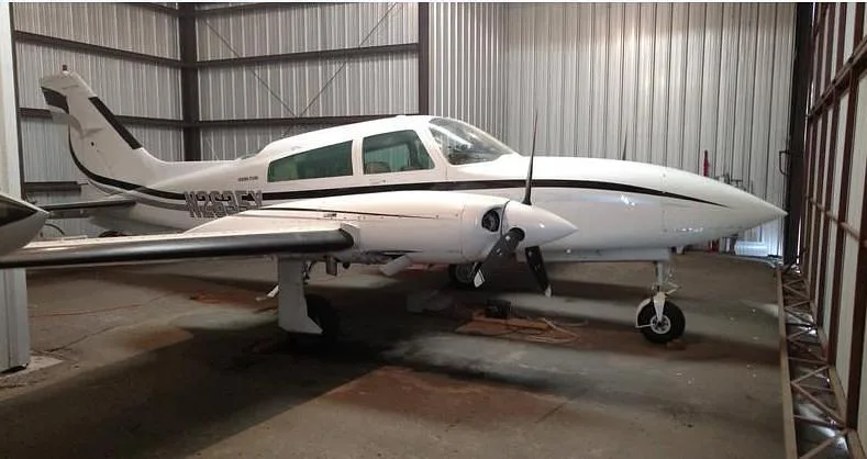 A white twin-engine aircraft, N2635X, with black and gray stripes, viewed from the front-right inside a hangar.