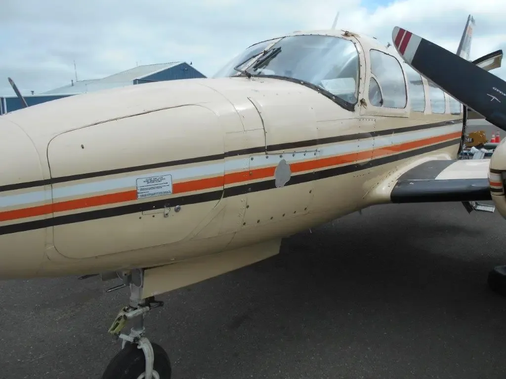 A close-up view of the nose and left side of the beige Piper Navajo aircraft, N4112E, highlighting the paint scheme.