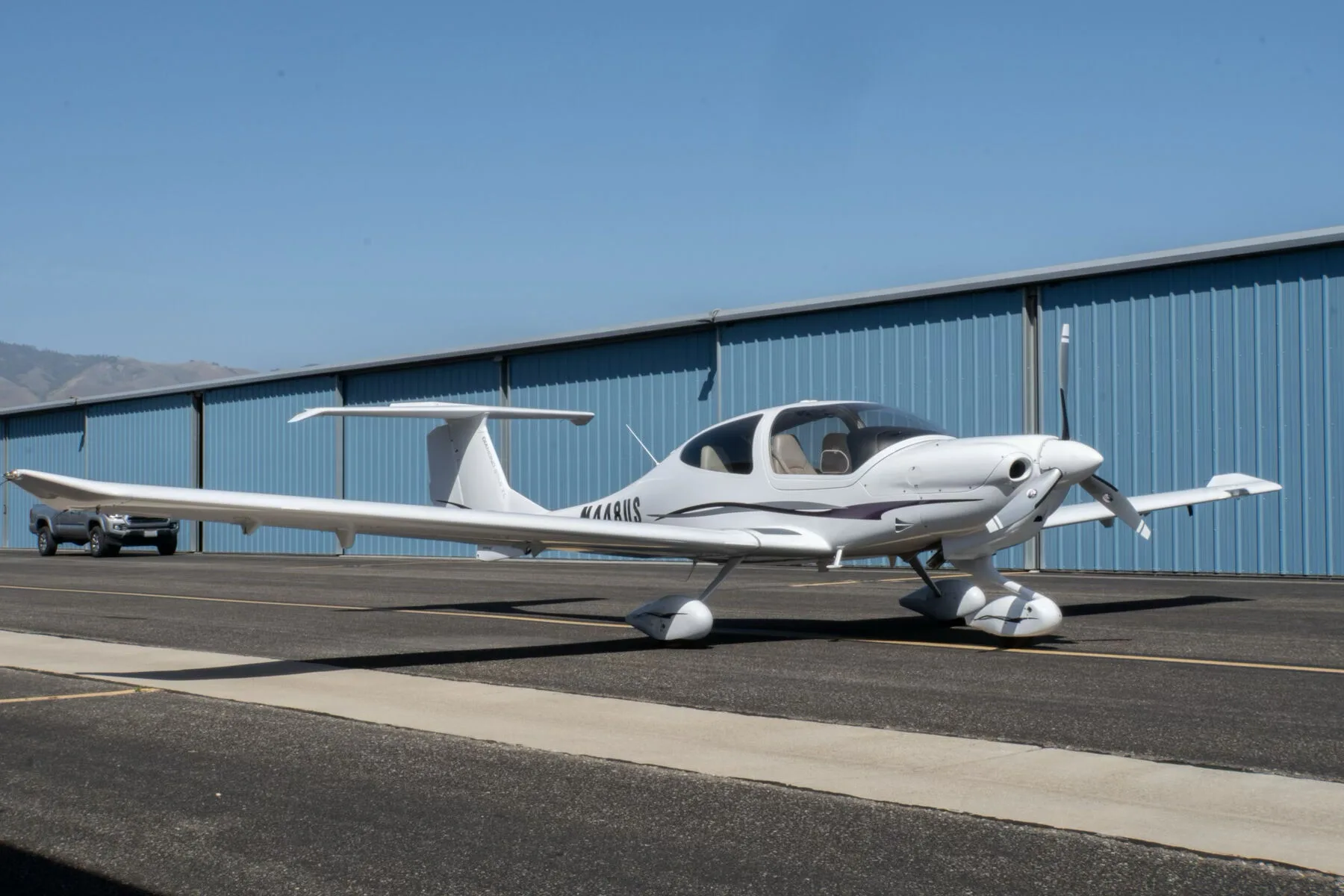 A white Diamond DA40 Star XL aircraft with purple and grey stripes, registration N448US, parked on an tarmac in front of a blue hangar.