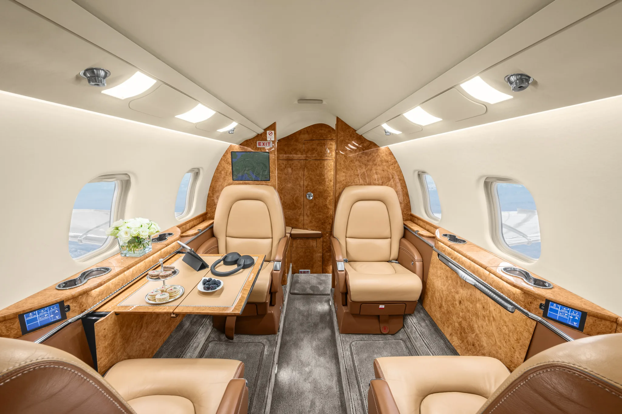 The luxurious interior cabin of a private jet, featuring two tan leather seats facing each other with a table set with snacks and headphones.