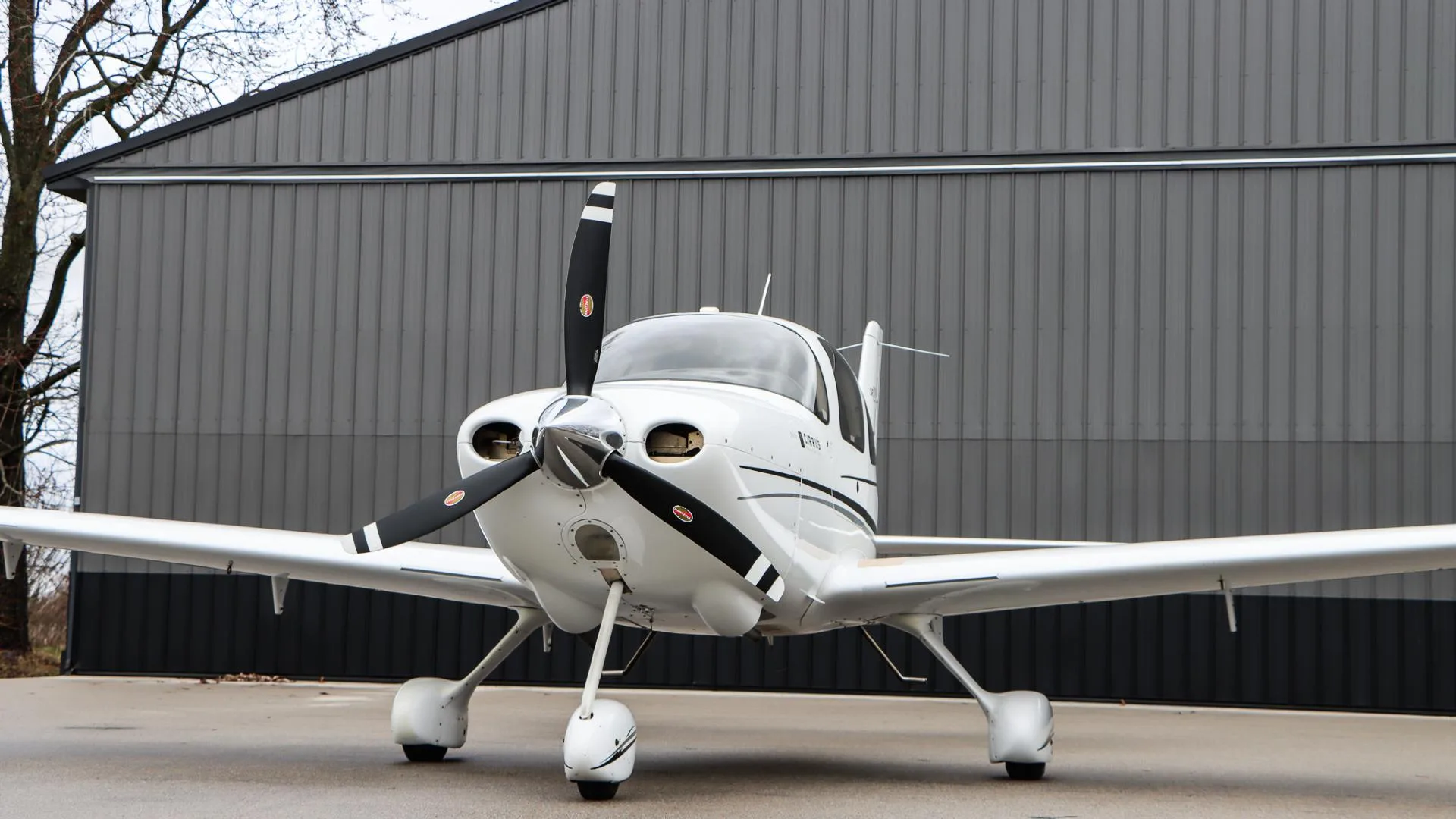 A white Cirrus SR20 GTS aircraft, N984PG, is parked at a slight angle in front of a dark gray hangar.