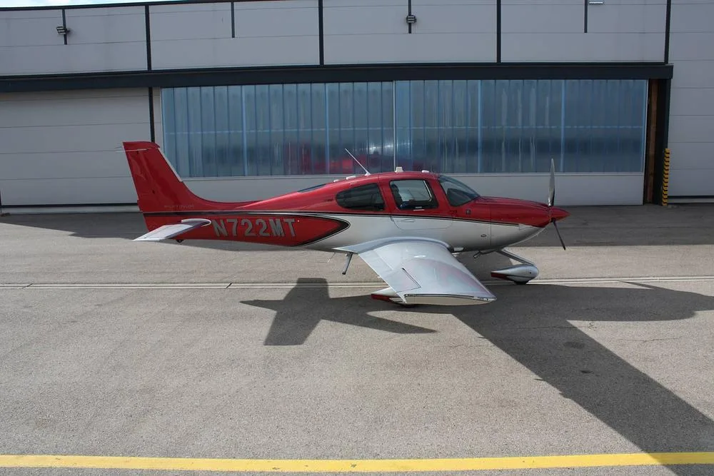 A red and white Cirrus SR22 aircraft, registration N722MT, parked on an asphalt apron, showing its left side.