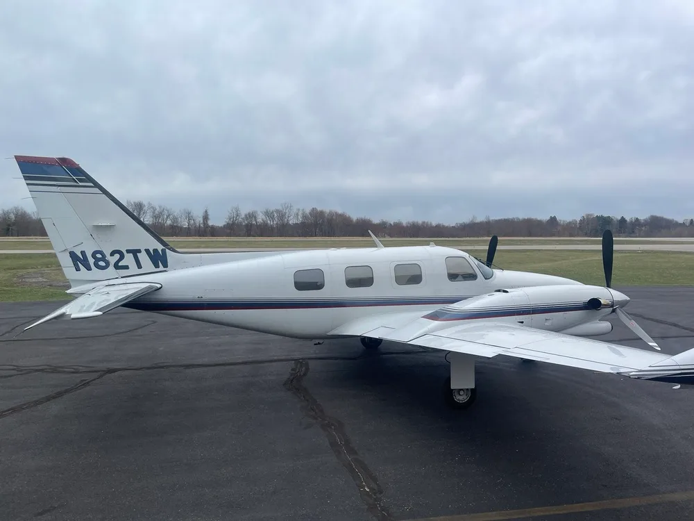 A side view of the white twin-engine aircraft N82TW, showing its dark blue and red stripe paint scheme and tail number, parked on a tarmac.
