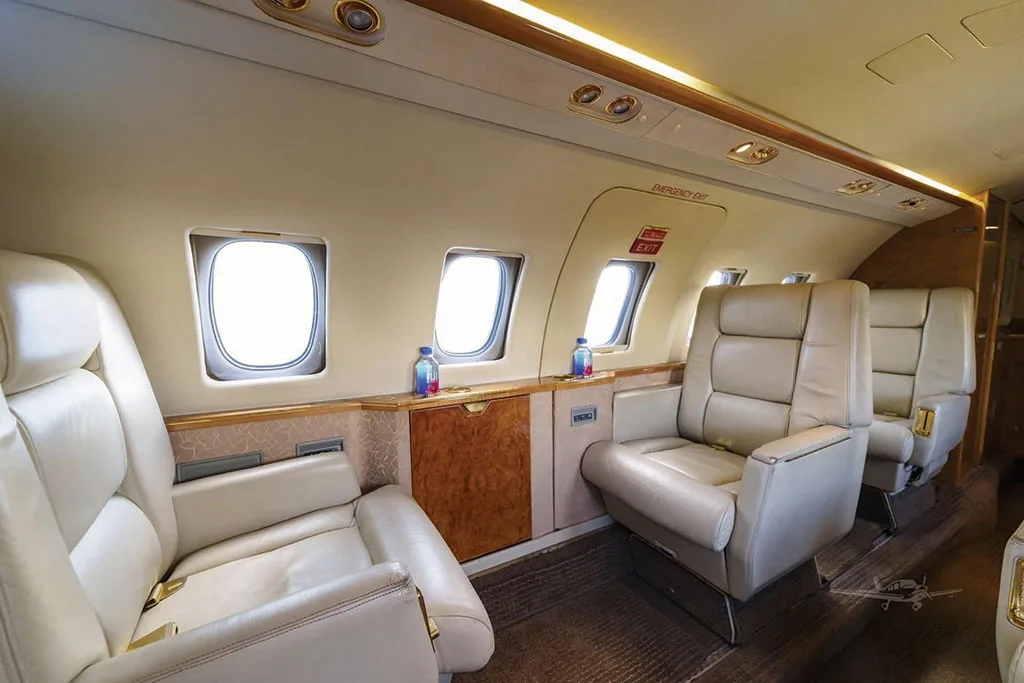 A side view of the Dassault Falcon 50's cabin, highlighting two beige leather club seats, large windows, and polished wood cabinetry.