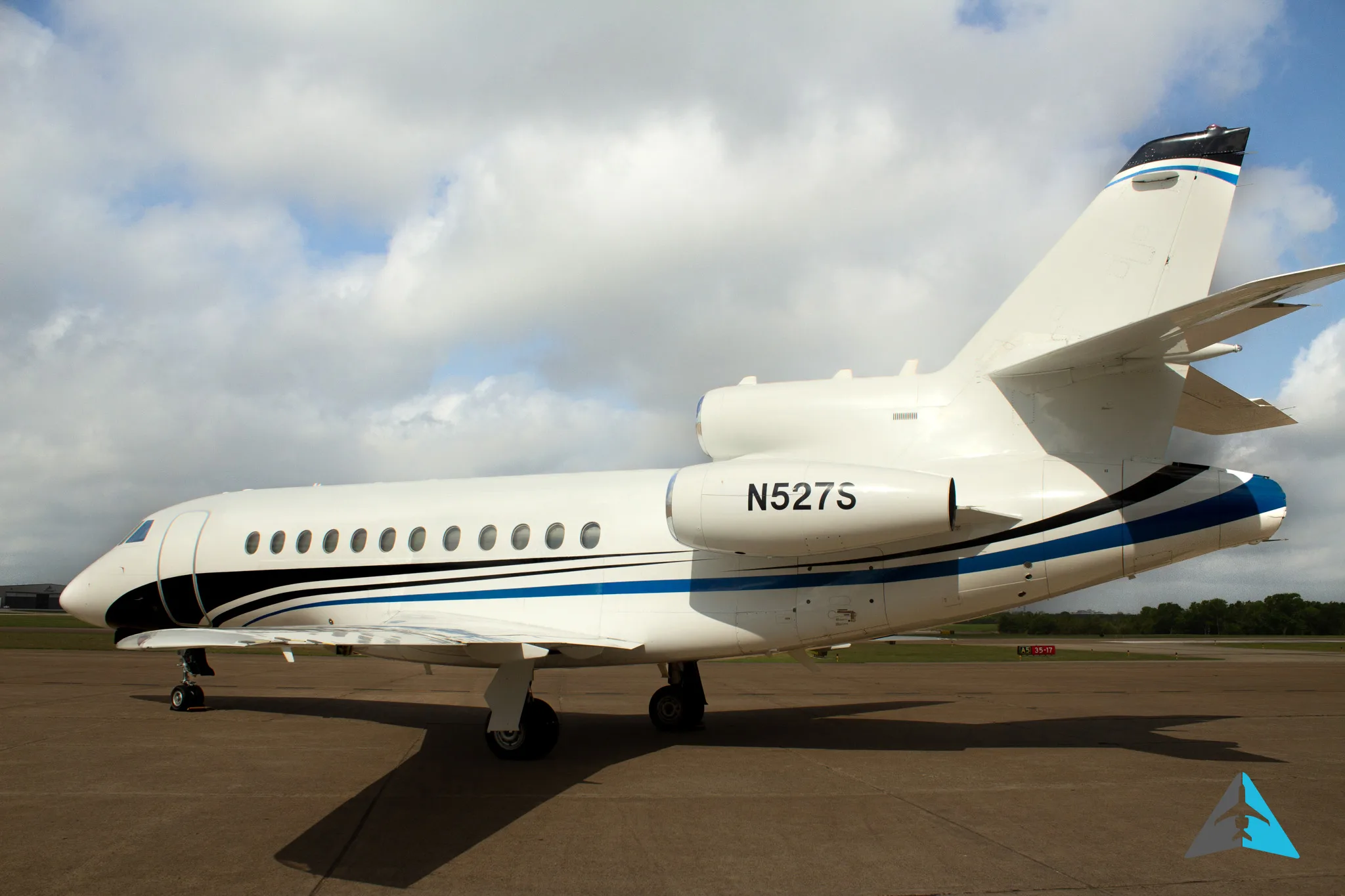 A rear-side view of a white Dassault Falcon 900EX business jet with black and blue stripes, parked on an airfield.