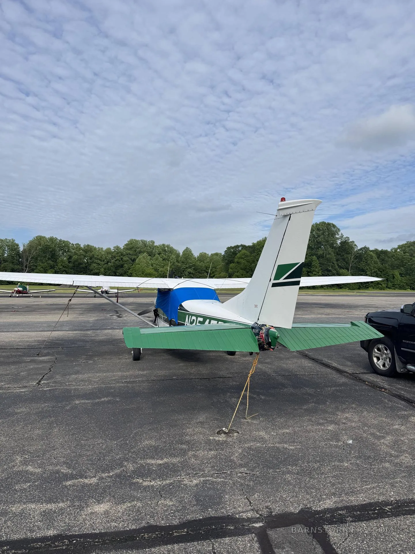 The rear view of a white and green single-engine propeller aircraft with a blue engine cover, parked on an asphalt ramp.