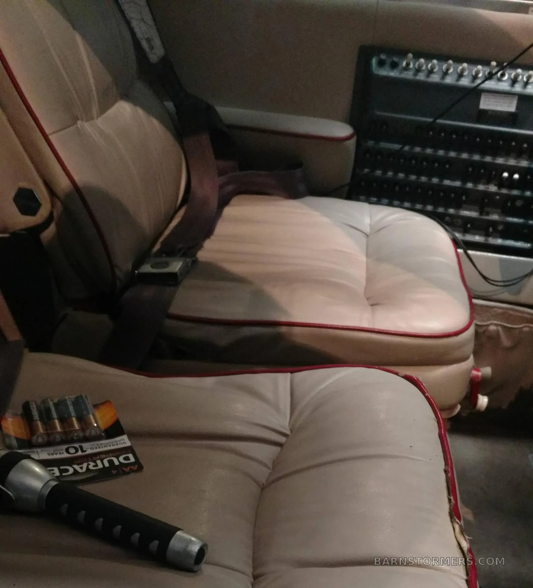 Tan leather aircraft seats with red piping, a flashlight, and batteries are visible inside the cabin.