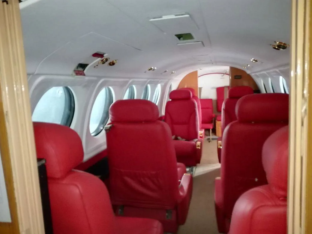 The aircraft cabin interior with red leather seats and large oval windows.
