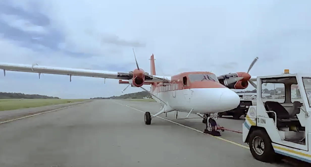 A red and white twin-engine turboprop aircraft is being towed on an airport tarmac under a cloudy sky.