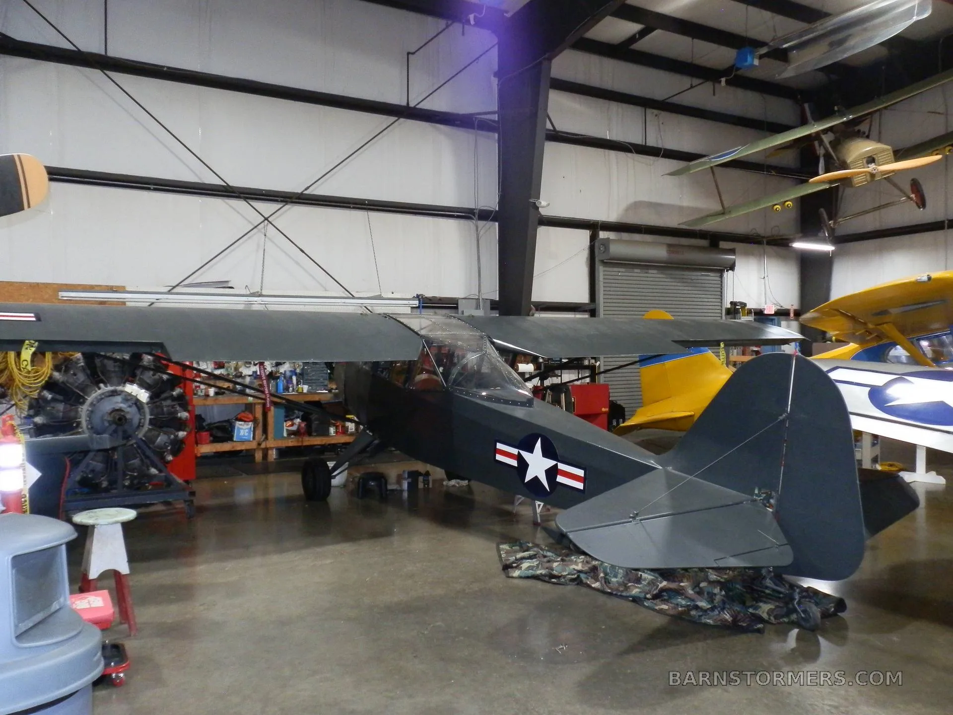 A dark grey single-engine taildragger aircraft with a US star insignia is parked in a hangar.