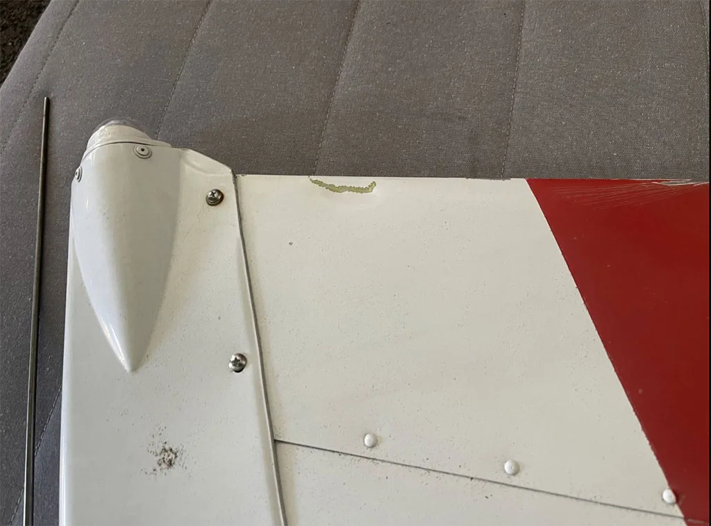 A close-up view of a white aircraft surface with a red stripe and a small area of paint damage.