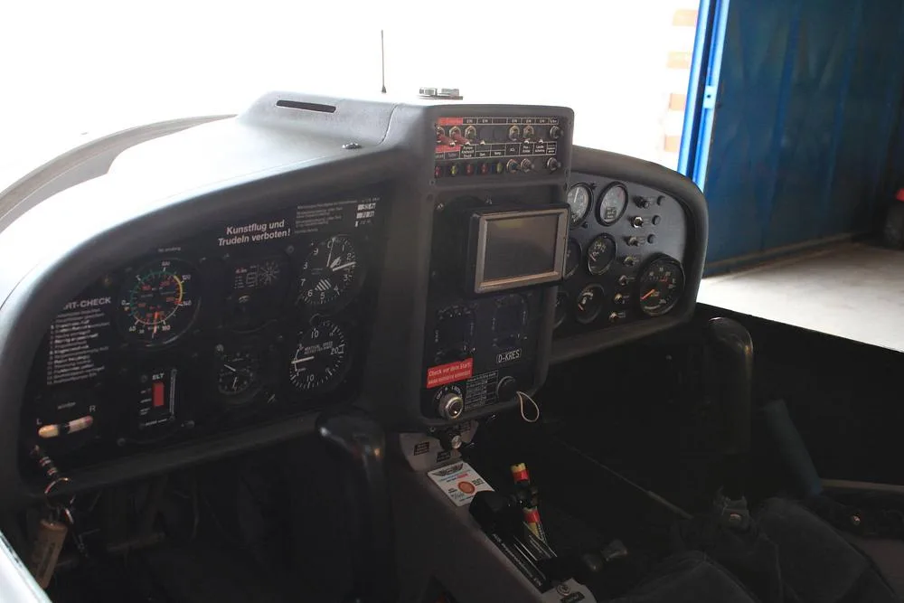 The cockpit of a light aircraft, showing the instrument panel with analog gauges and a small digital display.
