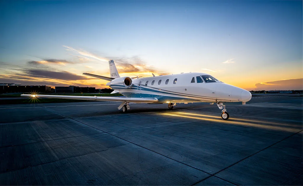 A Cessna Citation Latitude business jet, tail number N8701L, is parked on the tarmac at sunset.