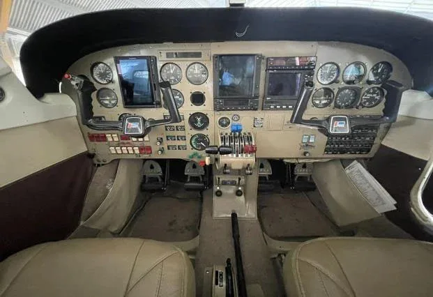 The cockpit of a small aircraft, showing the instrument panel with analog gauges and digital displays, and dual yokes.