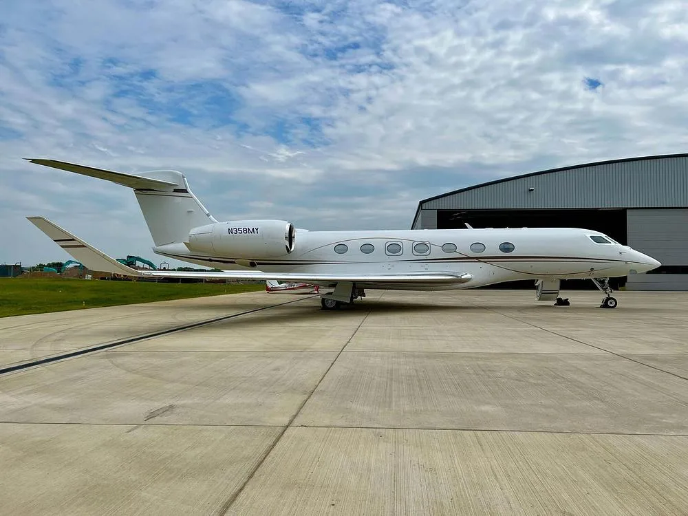 A white Gulfstream G650 business jet with tail number N358MY parked on a tarmac next to a hangar.