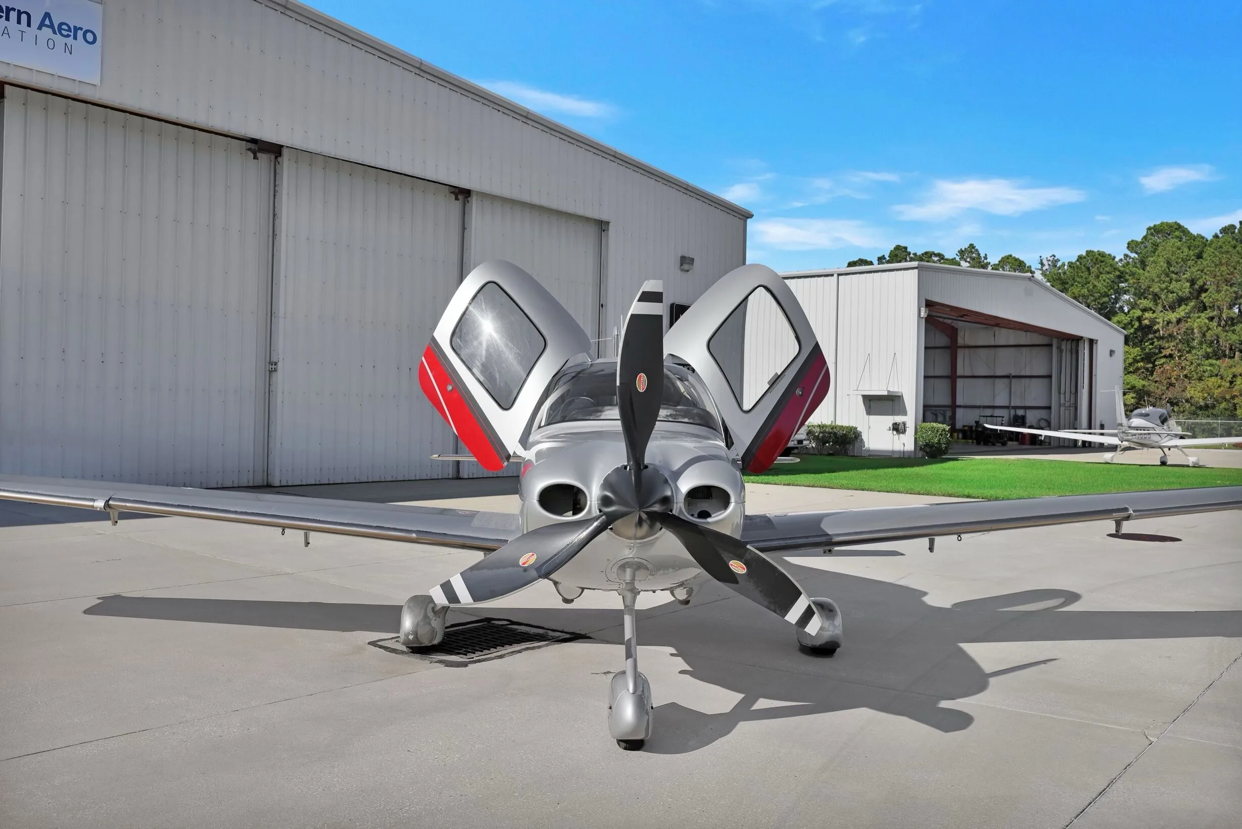 Front view of a Cirrus SR22T aircraft with red and silver paint scheme, registration N831MM, parked on an airfield with doors open.