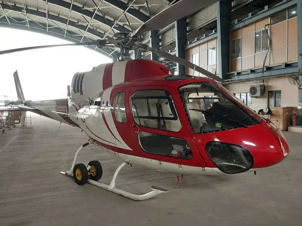 A red and white helicopter with a striped paint scheme parked inside a hangar, viewed from the front-right.