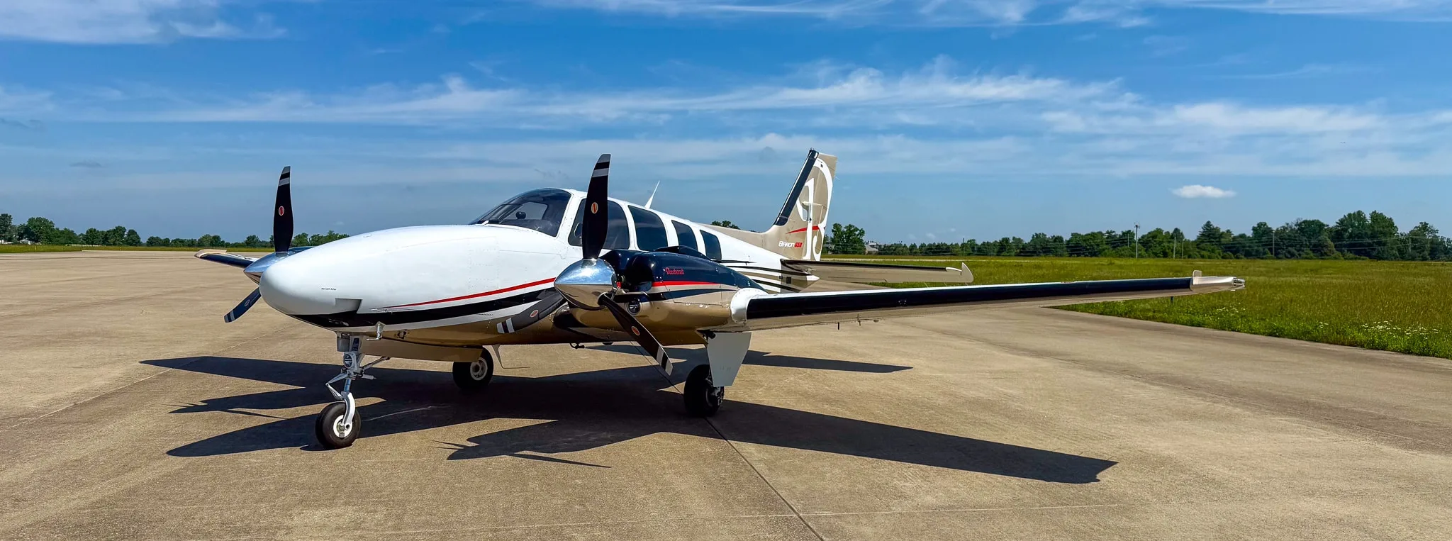Three-quarter front view of a white and gold twin-engine Beechcraft Baron G58 parked on an airfield.