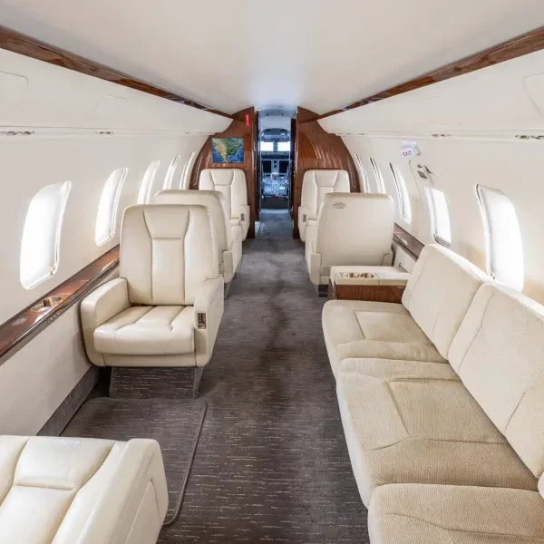 Long view of a private jet cabin with cream seats and a sofa, looking towards the cockpit.
