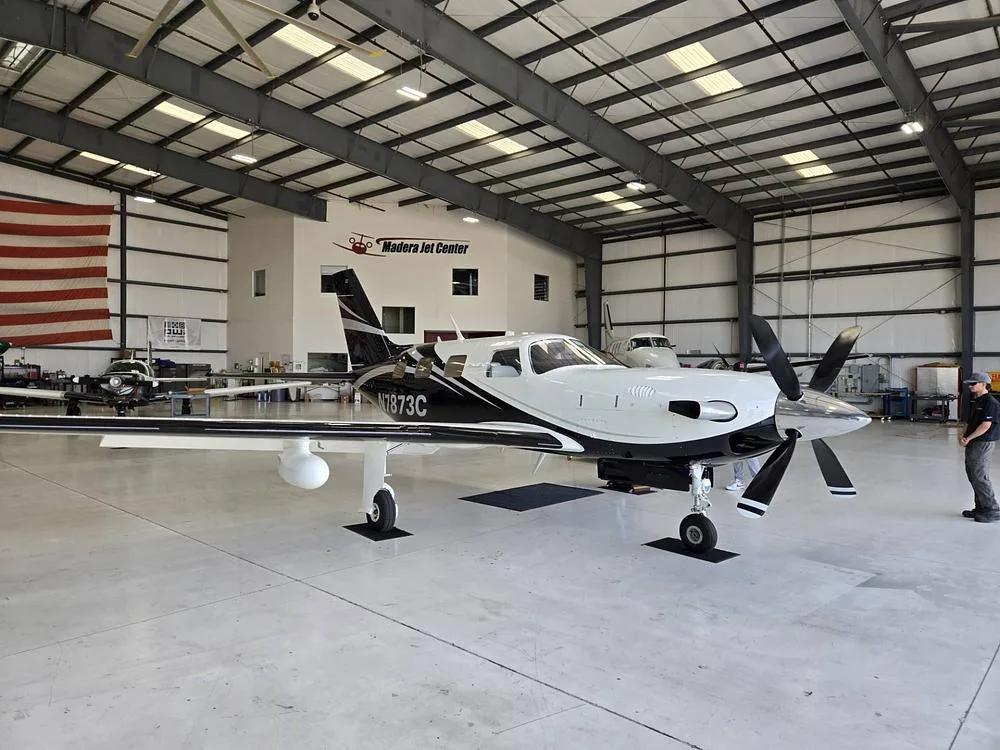 A black and white Piper Meridian aircraft, N7873C, is parked inside a hangar at Madera Jet Center.
