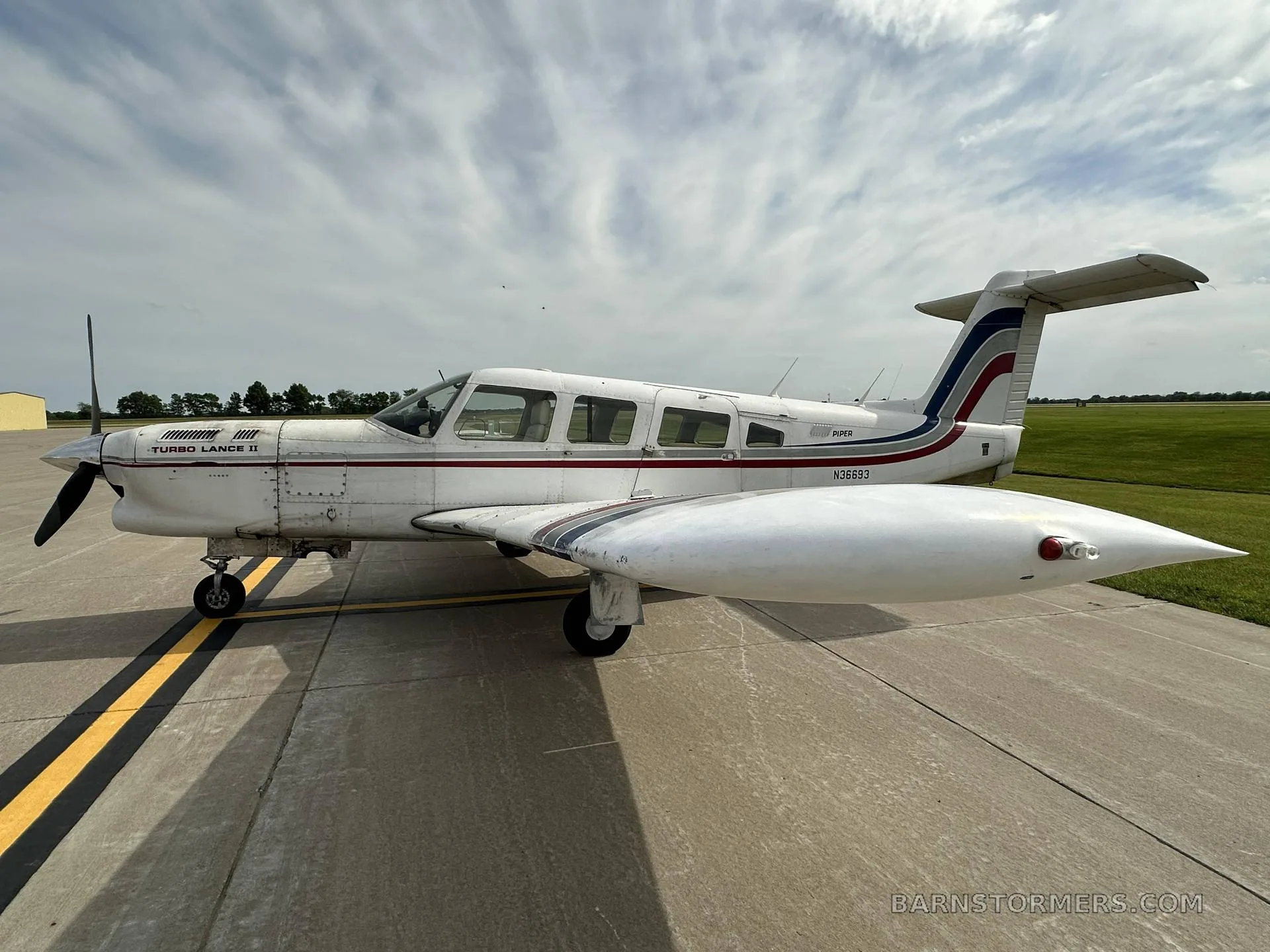 A side view of a white Piper Turbo Lance II aircraft with red and blue stripes and registration N36693, parked on an asphalt tarmac.