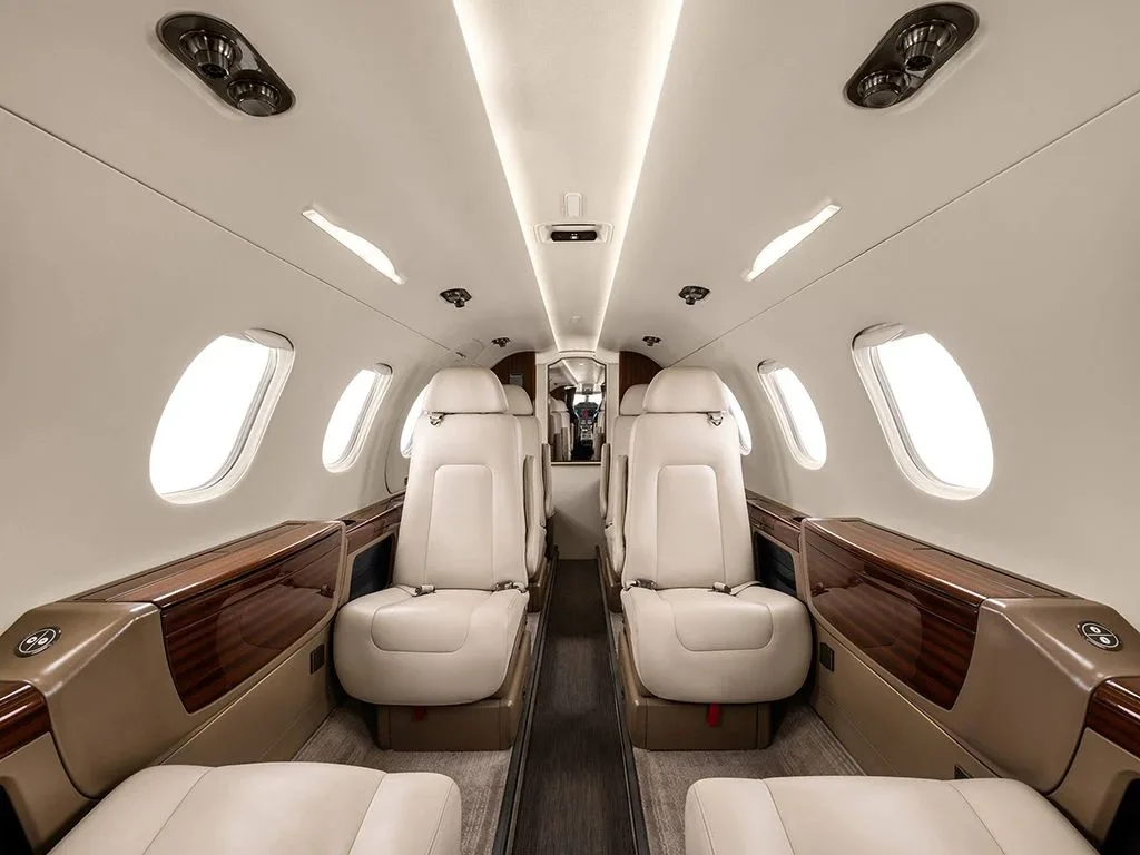 The luxurious interior cabin of an Embraer Phenom 300, featuring light cream leather seats and dark wood accents.