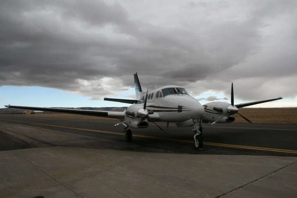 A white twin-engine turboprop aircraft with dark red and blue stripes on the fuselage and tail, parked on an asphalt runway under a cloudy sky.