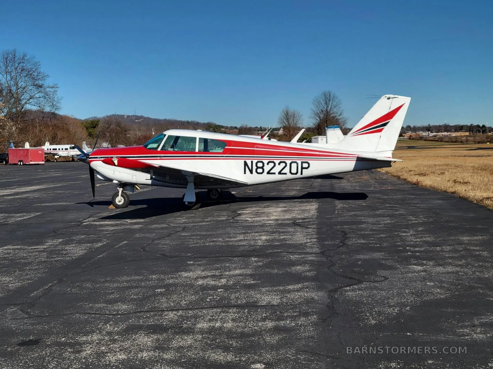 A white and red Piper Comanche 260 (N8220P) is parked on an asphalt ramp, viewed from the right side.