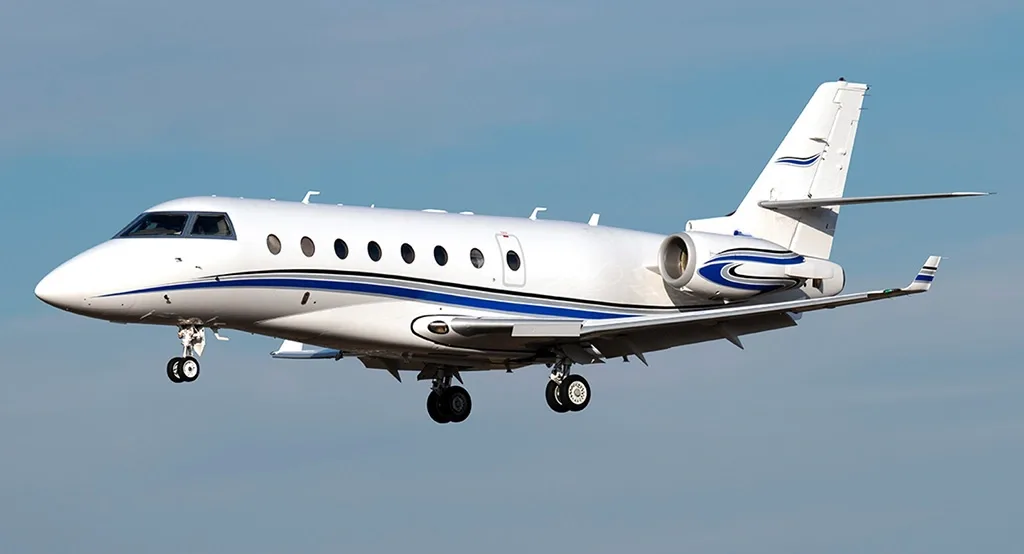 A white business jet with blue and black accent stripes on its tail and engines, in flight against a clear blue sky.
