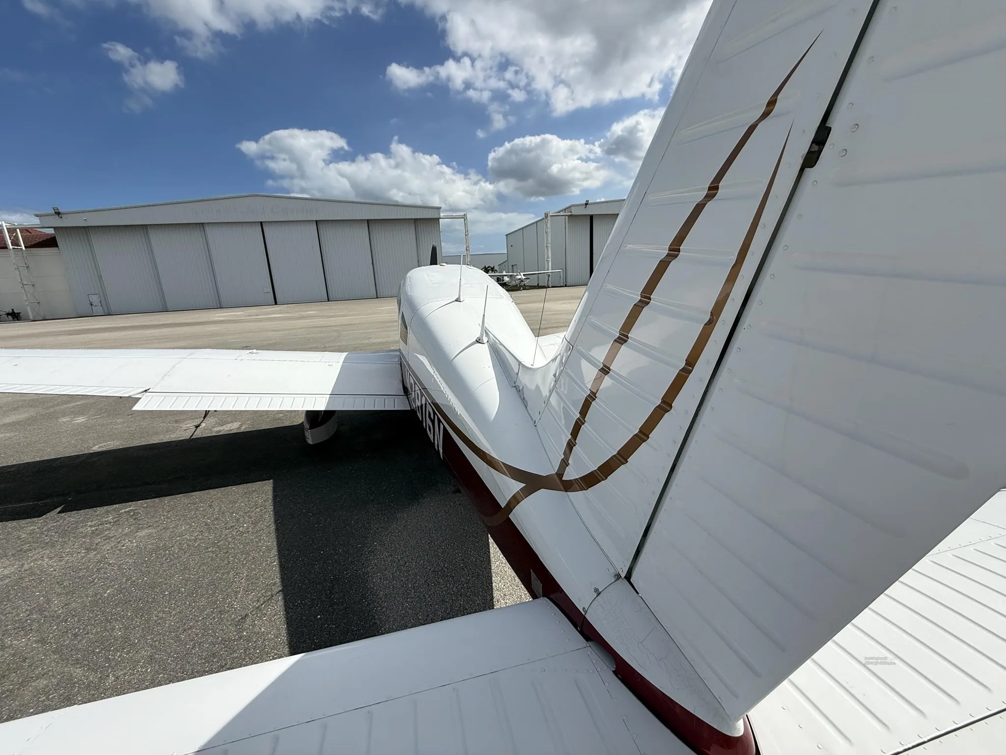 An overhead view of the tail section of a white and red Piper PA-28-161 aircraft, N2816N, with hangars in the background.