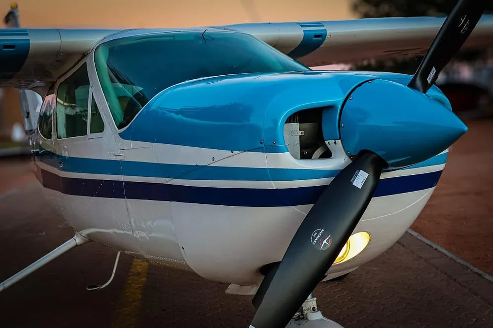 A close-up view of the nose and propeller of a white and blue Cessna 210 Centurion aircraft at sunset.