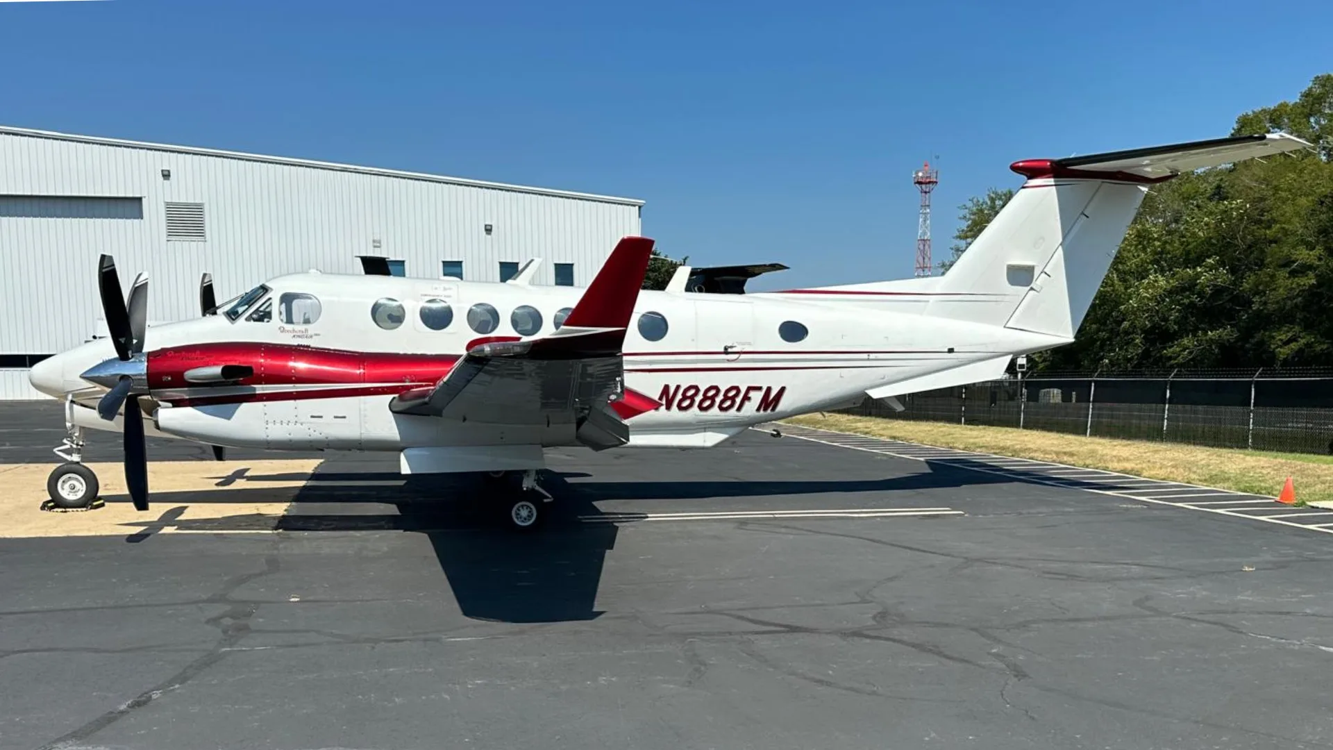 A white and red Beechcraft King Air N888FM parked on an asphalt tarmac next to a white hangar.