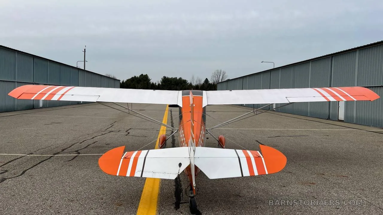 A rear view of an orange and white Cessna 170B aircraft with tail number N88319 parked on an asphalt apron.