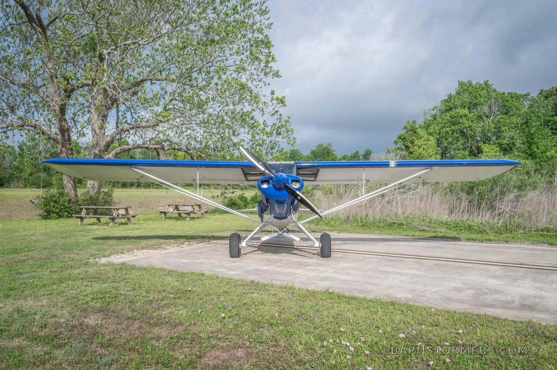 A blue and white single-engine taildragger aircraft (N6990R) is viewed from the front, parked on a concrete pad.