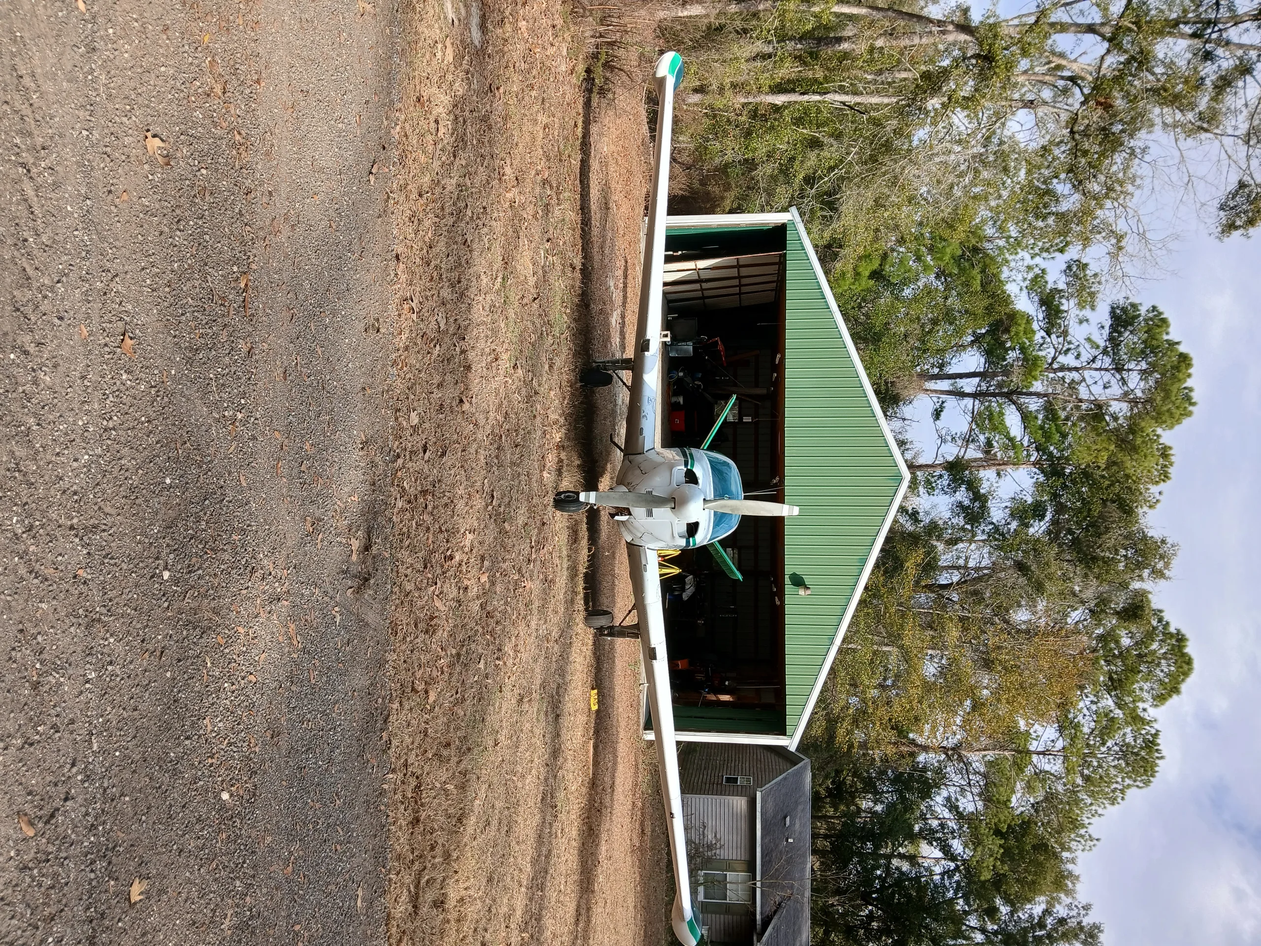 A white and green single-engine aircraft is parked head-on in front of a green hangar.