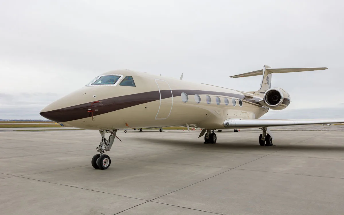 A tan and brown Gulfstream business jet is parked on an airport tarmac under an overcast sky.