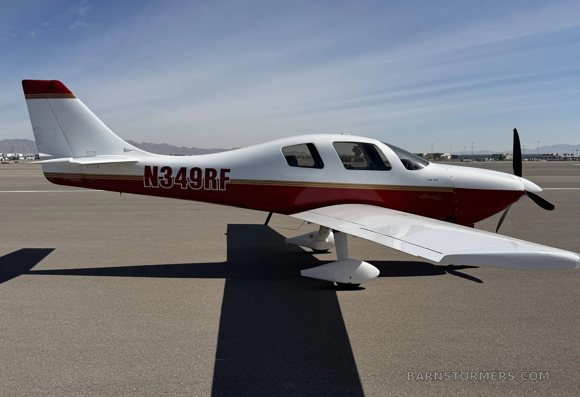 A white and red single-engine aircraft, N349RF, parked on an airfield under a clear sky.