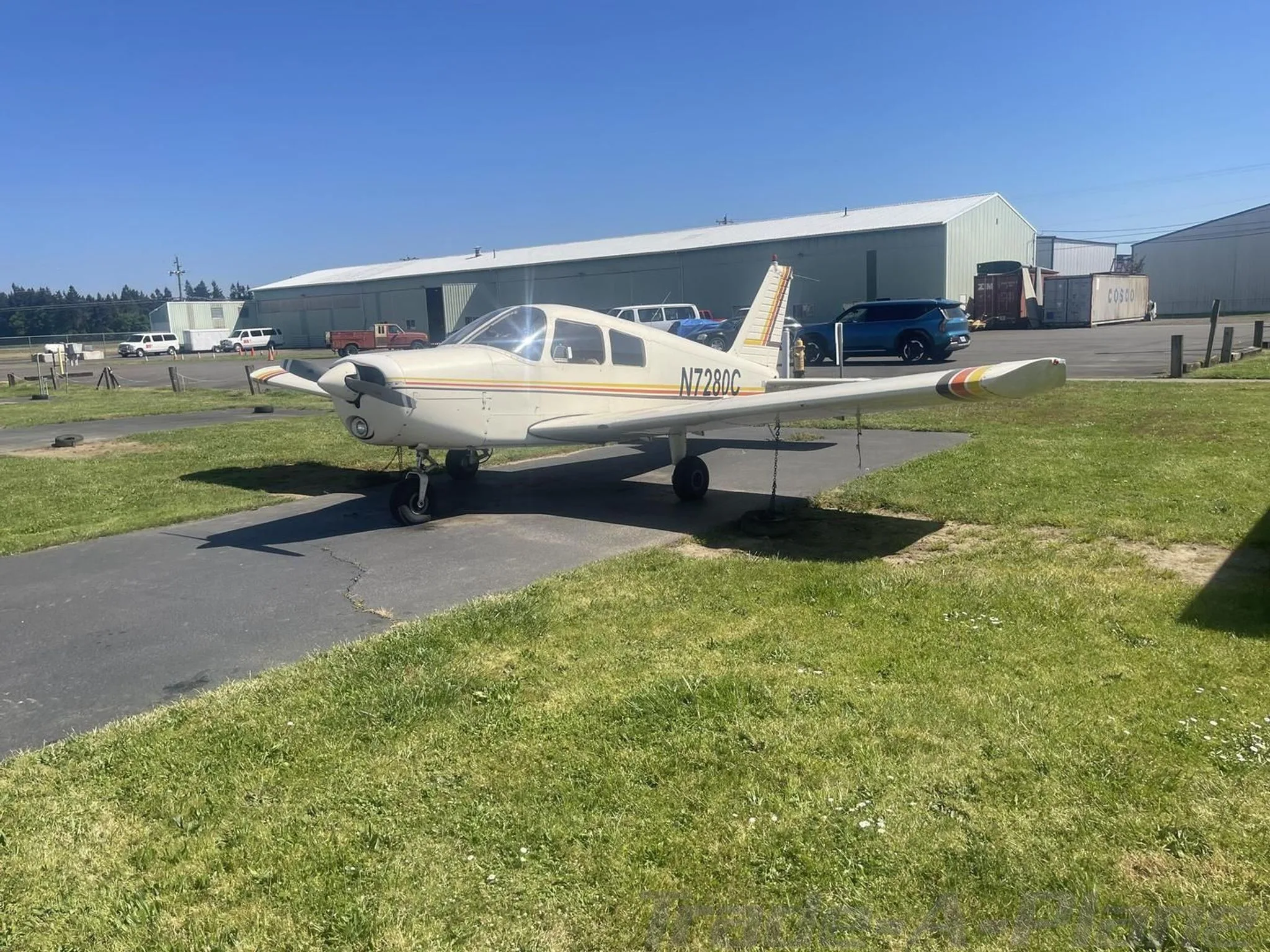 Side view of a white single-engine propeller aircraft with orange and yellow stripes, registration N7280C, parked on an asphalt strip.