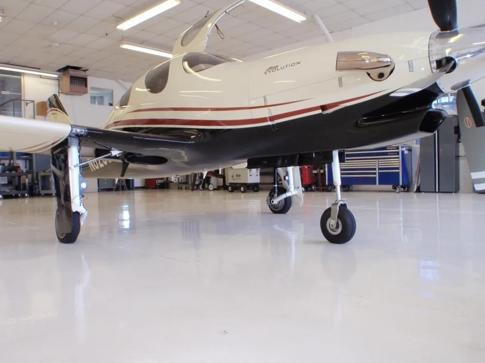 A low-angle view of a white and black Lancair Evolution aircraft with red stripes, parked in a hangar.