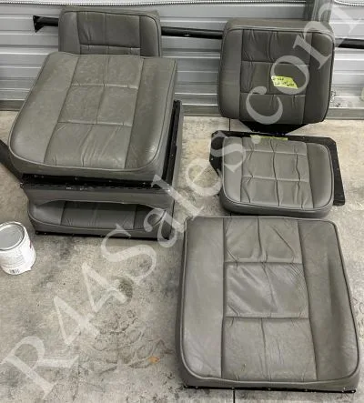 Several gray leather aircraft seats and seatbacks laid out on a concrete floor.