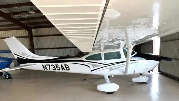 A side view of the white Cessna aircraft N735AB with black and grey accents, parked inside a hangar.
