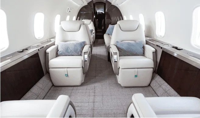 The luxurious interior cabin of a private jet features light-colored leather seats and a patterned carpet.