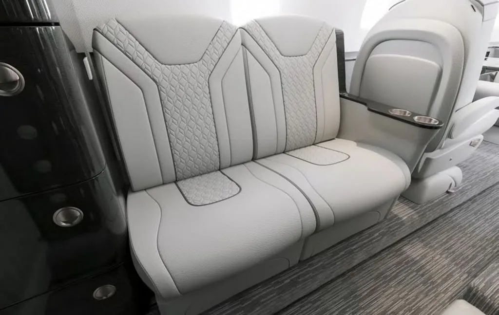 Close-up view of two light gray aircraft cabin seats with patterned upholstery and dark trim.