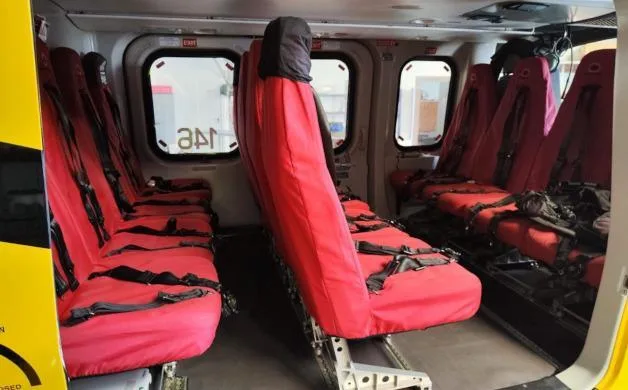 The interior cabin of a helicopter features multiple rows of red passenger seats.