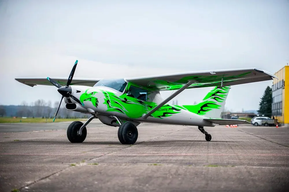 A white and green Backcountry Super Cub aircraft with a dragon paint scheme on an airfield tarmac.