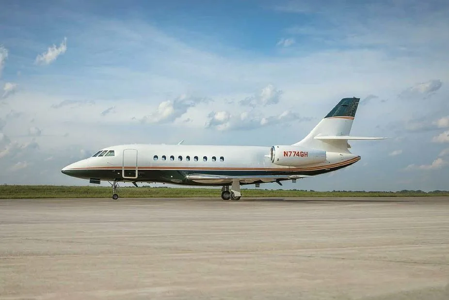 A Dassault Falcon 900EX business jet, registration N774GH, on a tarmac under a partly cloudy sky.